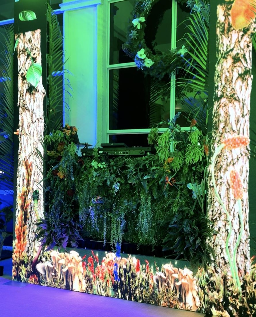 Forest-themed DJ booth framed by LED columns and lush greenery