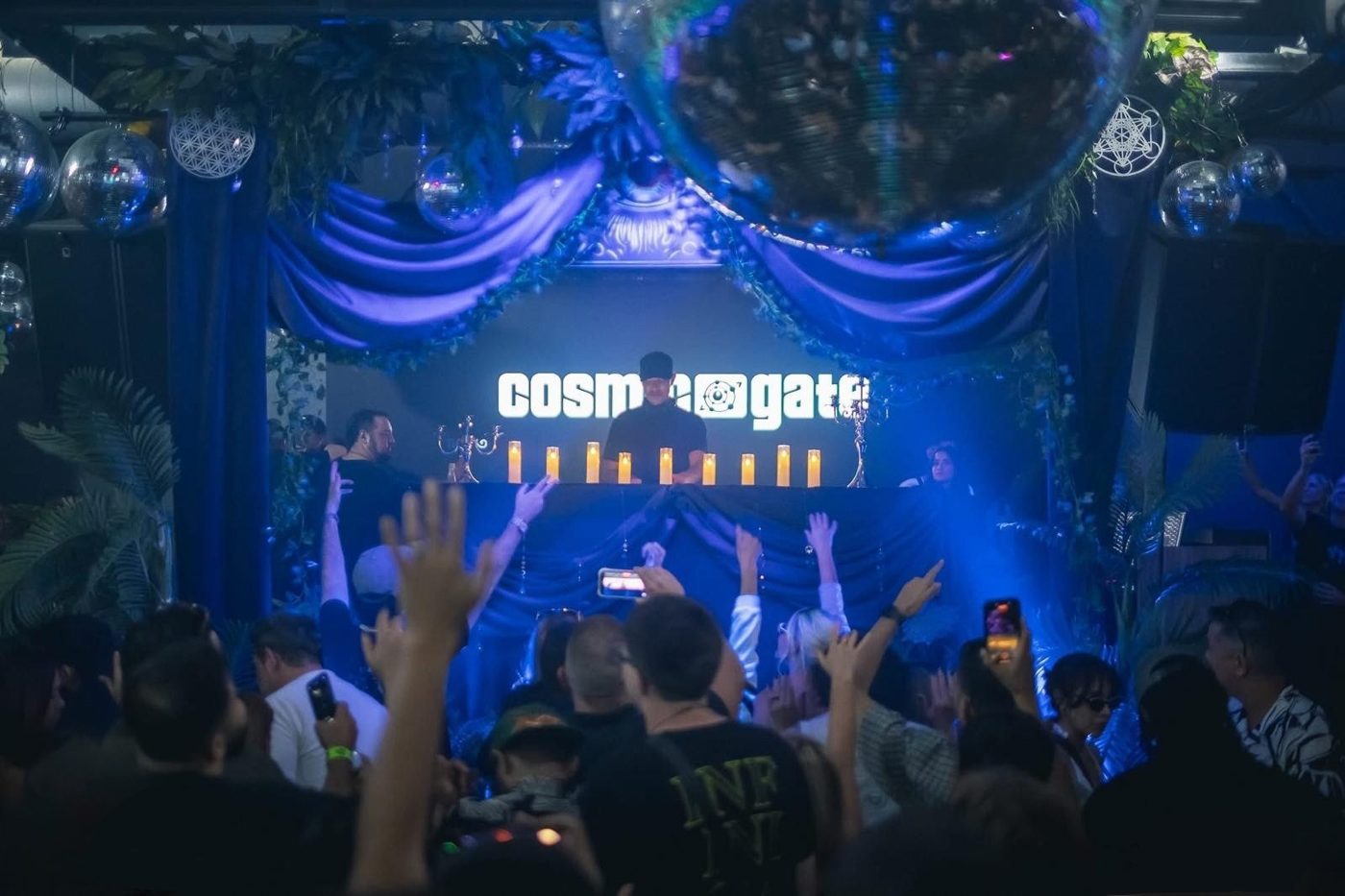 Cosmic Gate performing at a custom DJ booth with blue velvet drapes, candles and disco balls